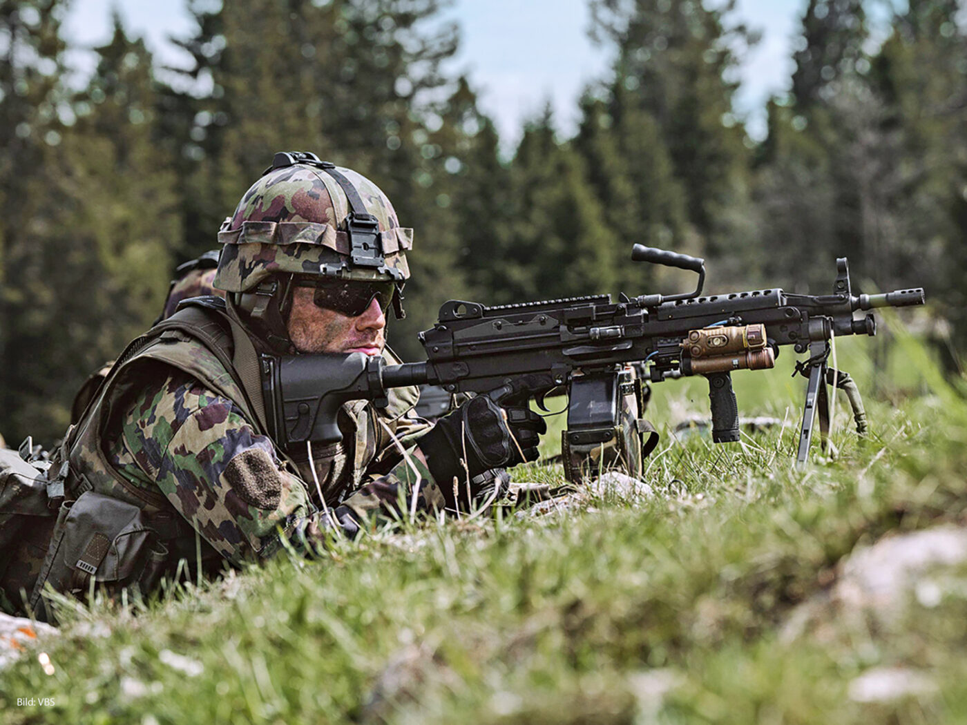 Soldat in Tarnuniform und Helm bei einer taktischen Übung im Freien. Der Soldat liegt am Boden mit einem Leichten Maschinengewehr 05 (LMg 05). Key Visual CD Armee.